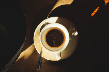 tazzina ripiena di caffè espresso e caldo, nell'ombra, illuminata in parte da un fascio di luce...
