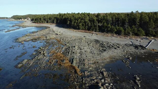 Aerial drone flight along the rocky and sandy shoreline of the vast St. Lawrence River, revealing forested landscapes near Pointe‑Leggatt in M&eacute;tis‑sur‑Mer on Quebec&rsquo;s Gasp&eacute; Peninsula.