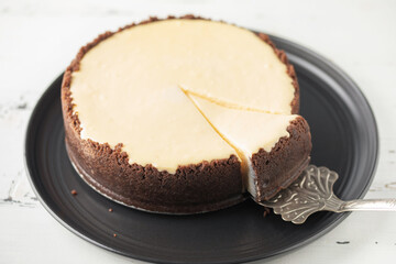 Tasty homemade cheesecake in ceramic plate on white wooden table.