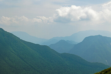 dettaglio di varie catene montuose nelle Alpi italiane che si estendono in lontananza verso l'orizzonte, avvolte da una fitta foschia e con un cielo nuvoloso