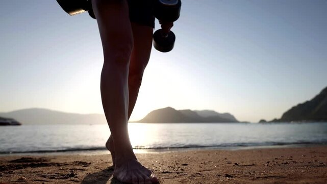 A woman performs an exercise with dumbbells on a sandy beach by the sea, her pose emphasizes muscle tension, and the sun illuminates her figure and creates an atmosphere of freedom.