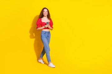 Full body photo of attractive young woman hold device walking dressed stylish red clothes isolated on yellow color background