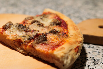 fetta di pizza margherita fatta in casa, con pezzi di salsiccia, vista da vicino e di lato, su un tagliere di legno