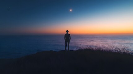 Silhouette of a young man contemplating the horizon at sunset by the ocean.