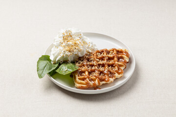 Croffle with whipped cream, basil leaves and caramel on a white plate. A trendy dessert or breakfast.