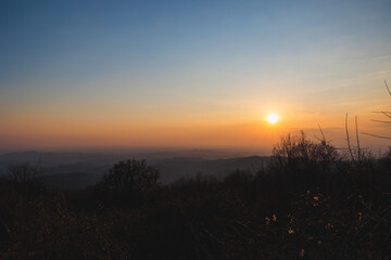 ampia vista panoramica di un ambiente naturale che si estende dalle colline slovene alla vicina pianura italiana, sotto un cielo sereno ed azzurro, colorato di arancione dalle luce del tramonto