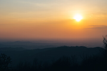 sole che tramonta all'orizzonte, dietro ad un fitto ammasso di nuvole e alla nebbia, colorata di...