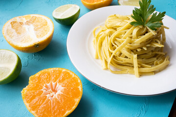 Close-up of linguini spaghetti pasta with pesto sauce on white plate with citrus fruits on the side