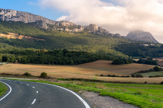 A winding road navigates through a lush, sunlit valley toward imposing rocky mountains, capturing a serene but adventurous pathway in a picturesque landscape in Navarra Spain
