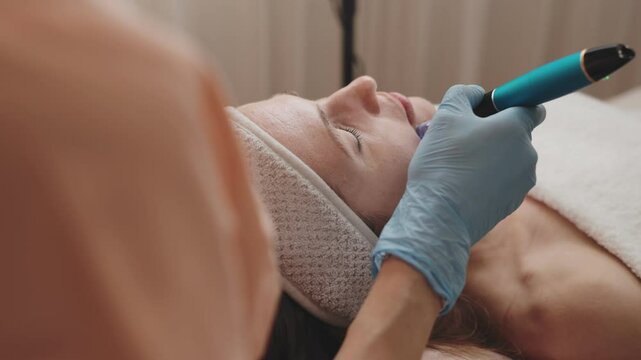 A skilled cosmetologist uses a derma pen on a client's face during a micro-needling therapy session to rejuvenate the skin.
