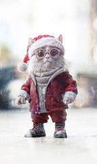 Portrait photo of a realistic cat with glasses dressed in a red wooly costume as santa claus on a snowy street  background