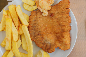 vista dettagliata da sopra di un piatto con una cotoletta di carne impanata accompagnata con delle...
