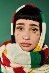 A young woman with short hair and tattoos embraces a warm sweater and scarf, in a studio.