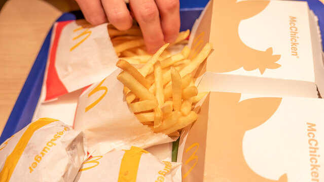 Hand picking up french fries from fast food tray with Mcdonald's burgers and mcchicken boxes closeup detail casual dining concept, unhealthy eating, lots of food on a tray