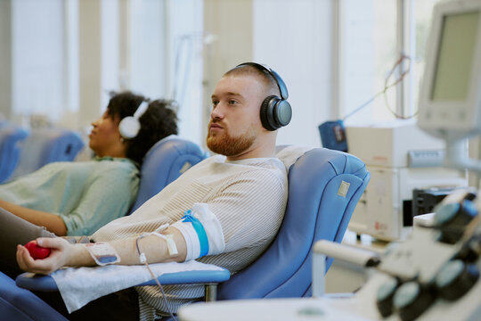 Group of people participating in blood donation in comfortable seating with modern medical equipment. Portrait of man looking at camera, holding stress ball, while donating