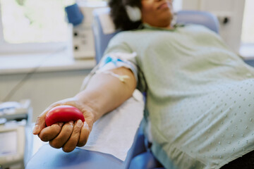 Close-up of person donating blood while squeezing a red ball. Patient in medical chair with...