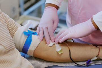 Medical professional wearing pink gloves taking blood sample from patient's arm with blue...