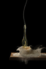 Huevo cayendo sobre harina salpicando con fondo negro