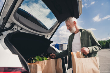 Photo of cheerful positive guy dressed khaki shirt putting shoppers vehicle outdoors urban city...