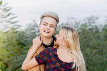 close-up a beautiful young blonde lesbian couple in summer walking near the water tenderly hugging...