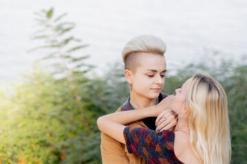 close-up a beautiful young blonde lesbian couple in summer walking near the water tenderly hugging...