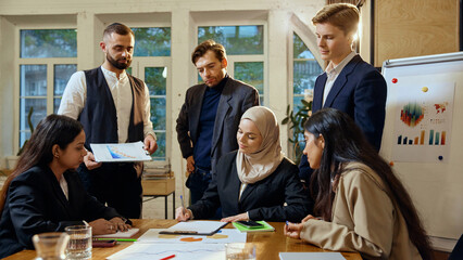 Multicultural team of business people gathered in modern office space, actively engaging in strategy presentation. Working with data charts and analytics. Concept of dei in business, teamwork