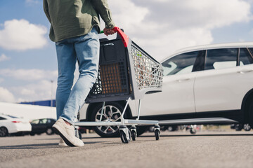 Cropped photo of walking senior man putting paper bags food car trunk shopping cart mall parking...