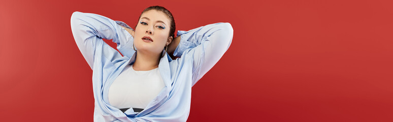A young plus size woman showcases vibrant makeup and style, posing effortlessly on a striking red...