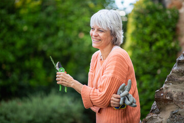Senior woman smiling while holding pruning shears and gardening gloves