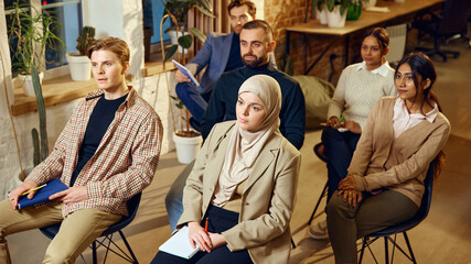 Multiracial group of business people listening attentively during seminar in modern workspace. Corporate learning in dynamic environment. Concept of dei in business, teamwork