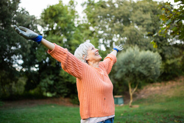Happy elderly woman enjoying the outdoors with arms raised in a garden