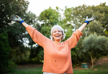 Cheerful elderly woman with arms raised outdoors in a garden