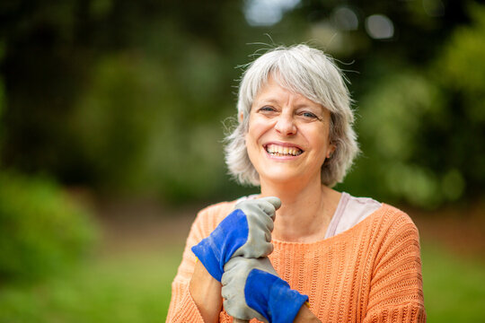 Senior woman smiling in garden while wearing gardening gloves