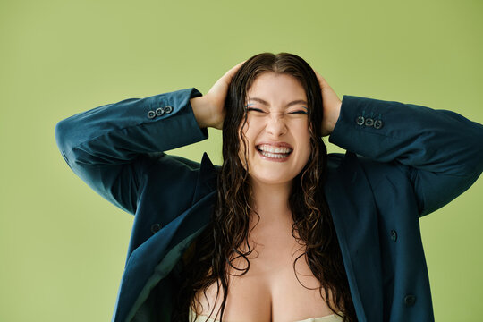 A cheerful plus size woman with curly hair enjoys a fun pose while wearing a chic suit in a studio setting.