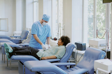 Nurse assisting patient during a blood donation process in medical clinic with modern equipment and...