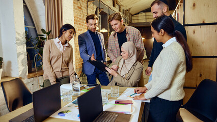 Multicultural team discussing ideas around table, involved in brainstorming session. Diverse group focused on shared goals and ideas, representing inclusive business practices. Concept of dei business