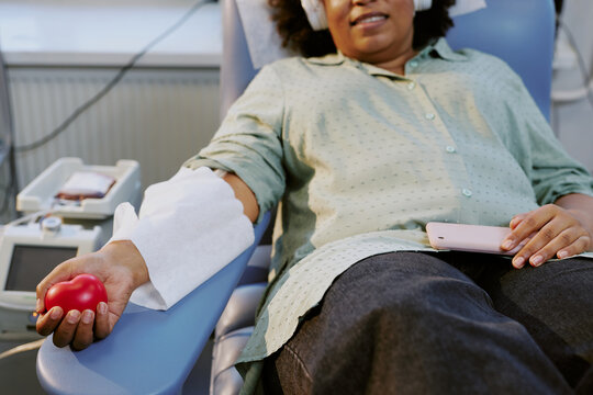 Person lying comfortably while donating blood in modern medical facility. Patient holding stress ball with bandage on arm, suggesting calm and cooperative feeling