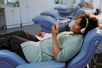 Woman listening to music using headphones and holding smartphone while reclining in a dental chair...