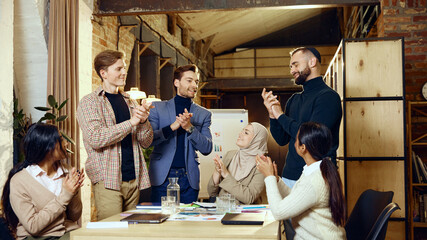 Colleagues from various cultural backgrounds applaud one another around conference table, showing appreciation and encouragement. Concept of dei in business, teamwork, corporate culture