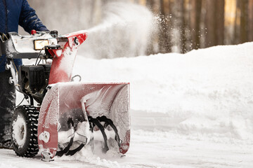 A man with a red snowplow clears the territory from snow. Clearing the territory from snowfall. Selective focus