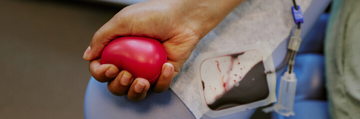 Hand holding heart-shaped squeeze ball while donating blood via intravenous drip. Close-up...