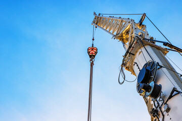 A large construction crane with cables extending against a clear blue sky,  White crane arm and hanging cables captured from below,  illustrating industrial work and heavy lifting. Copy space