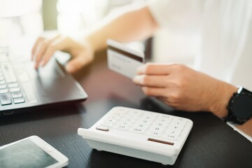 Close up man hands holding credit card and using laptop computer. Doing online shopping on internet store. Entering information of banking service and making secure payment.