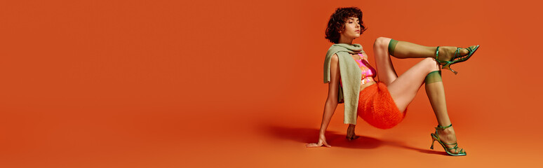 A young woman showcases her emotions while seated stylishly against a bold orange background.
