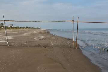 Wire mesh fencing on a sandy sea beach. A fence blocks access to the beach. Caspian Sea, Iran