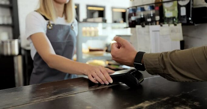 Man hand with smartwatch using terminal for payment, non-cash transaction, side view. Non-cash payment concept. Pos-terminal on table on black background.
