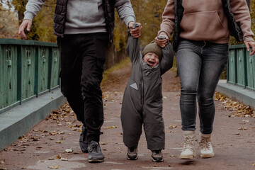 Mom and dad holding babys hands and having fun in the autumn park on the bridge