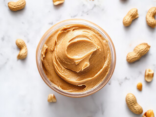Smooth peanut butter spread in a jar surrounded by peanuts and cashews on a marble surface.