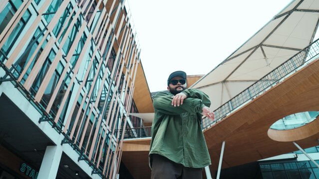 Low angle view of hipster pose in hip hop style surrounded by mall view. Portrait of sporty asian hip hop choreographer dancing break dance while looking at camera. Outdoor sport 2024. Hiphop. - Powered by Adobe