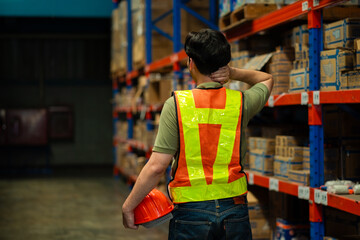 A man in a safety vest and helmet is walking through a warehouse. He is wearing a reflective vest...